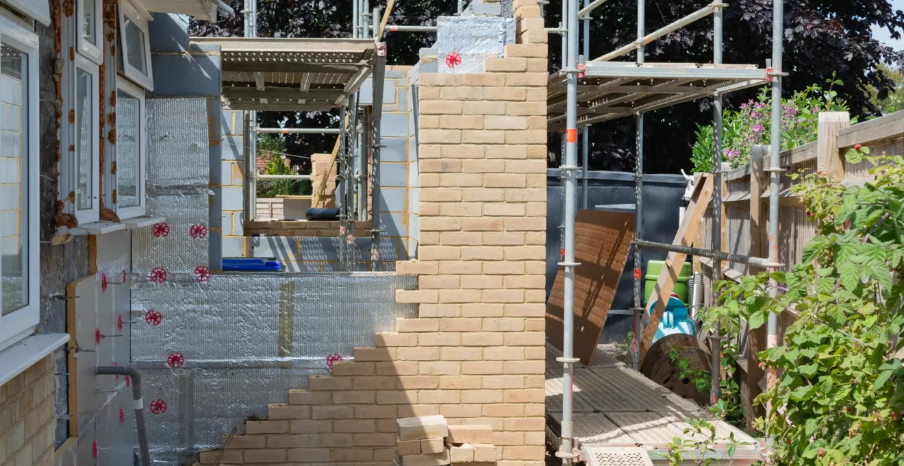 Mason's hands precisely positioning a stone block in a house extension wall.
